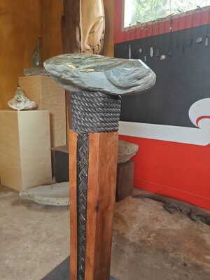 Carved pedestal table with a stone top, masks on the wall behind