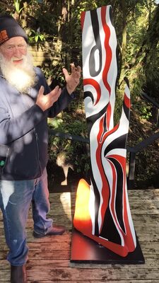 A carver beside a red, white and black carved sculpture at night