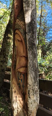 Carved post with a face and a green koru pattern on the chest